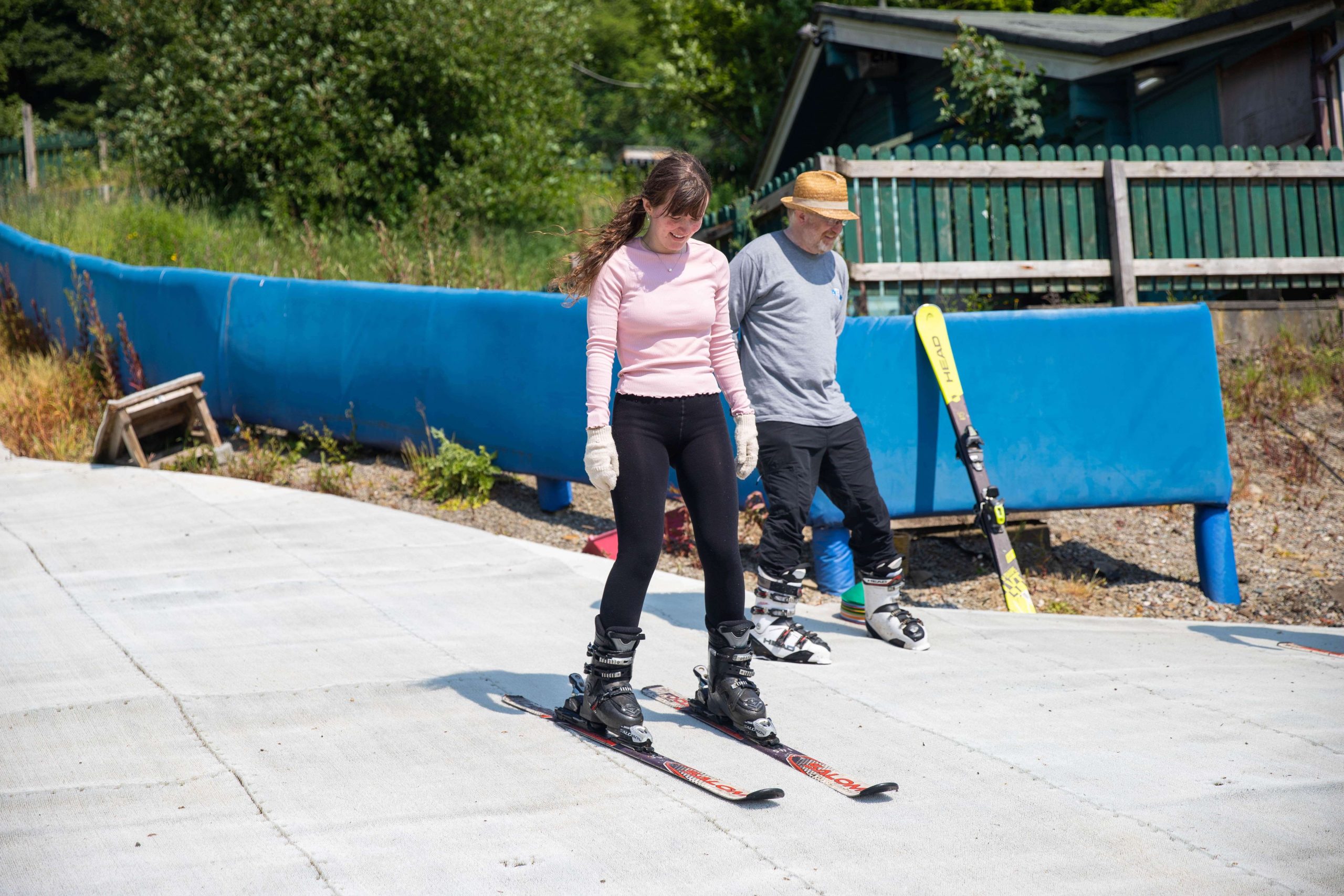 Learning the ropes: A beginner skier practices on the gentle slopes at Ski Rossendale, guided by an instructor. The bright summer day adds warmth to the experience, making it the perfect time for outdoor learning and fun on the dry ski slope.